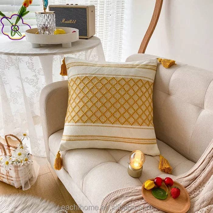 Mustard yellow and white tufted cushion cover with corner tassels displayed on a beige sofa