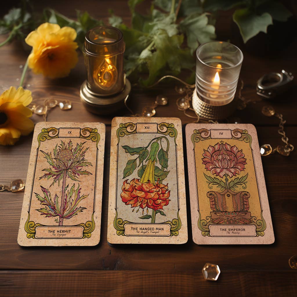 Three Botanica Oculta tarot cards displayed on a wooden tray with a lit candle and yellow flowers
