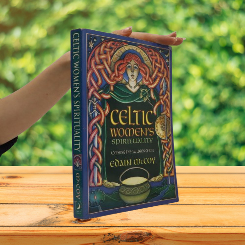 Hand holding the Celtic Women's Spirituality book upright on a wooden table outdoors