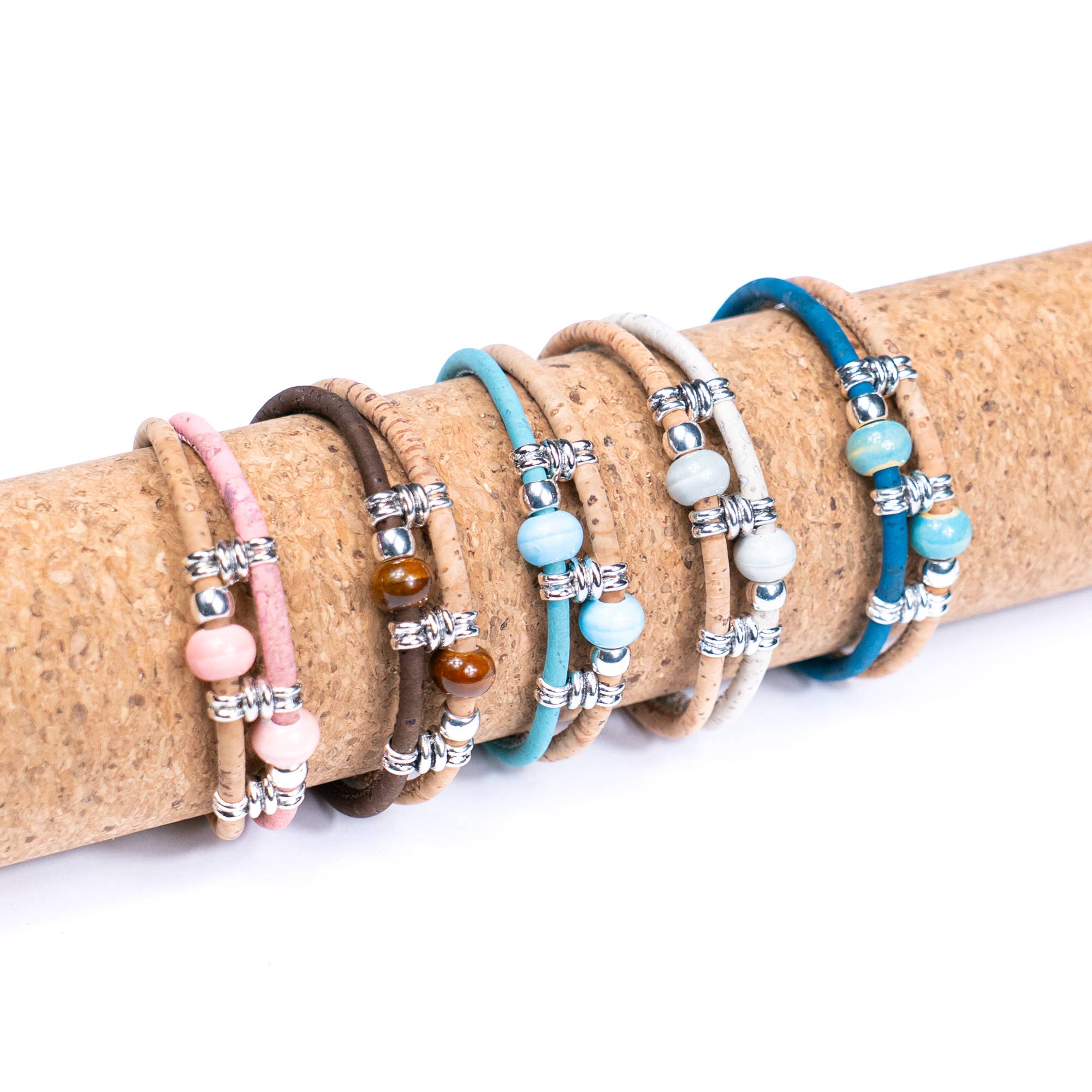 Meninas Bonitas Cork Colourful Ceramic Bead Handmade Bracelet 18x1cm – layout – five cork bracelets in dark brown, white, light blue, royal blue, and pink displayed on a cork roll.